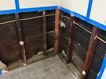 Wall corner with exposed water-damaged studs, yellow electrical wiring, and construction debris