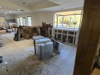 Interior room under renovation with concrete floor, HVAC equipment, treadmill, and opened wall exposing studs