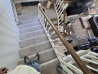 Top-down view from staircase showing living room with rug, leather sofa, coffee table, and TV during site inspection