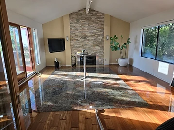 Flooded living room with standing water on hardwood floors, vaulted ceiling, stone fireplace, and extraction equipment