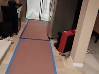 Hallway with floor protection paper, blue painter's tape, plastic containment barrier, and red air mover