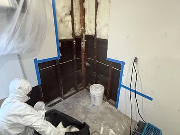 Save Pro technician in full PPE suit removing damaged insulation from an opened wall cavity