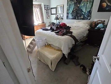 Bedroom during restoration inspection with wall-mounted TV, bed, and ceiling access panel visible