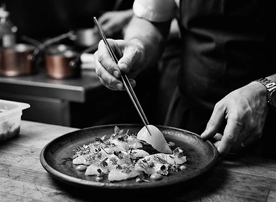 The Chef's hands plating fish with herbs