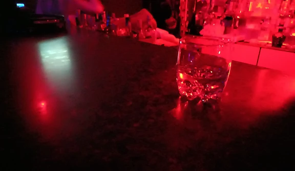Amber drink over ice on a reflective bar top in red light