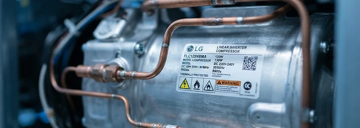 LG inverter compressor close-up — brushed metal and copper piping in cool blue light