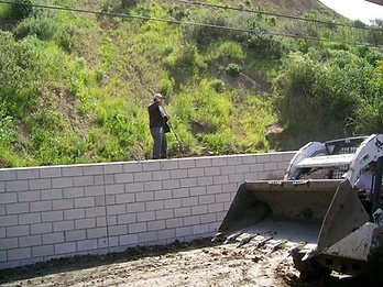 Worker and skid-steer loader installing a concrete block retaining wall