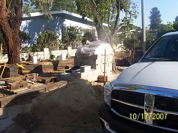 Construction site with sand pile, miter saw, concrete blocks on landscape timbers, and white truck staged near a residential property