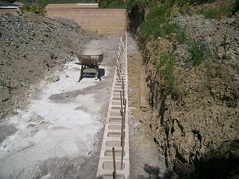 High-angle view of concrete masonry units and vertical rebar laid in a trench for a retaining wall foundation