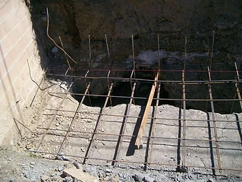 Top-down view of rebar reinforcement cage in a trench with red mason line, wooden support, and existing block wall section