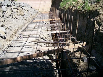 Rebar reinforcement cage laid in an excavated trench with vertical starter bars and wooden bracing for a retaining wall foundation
