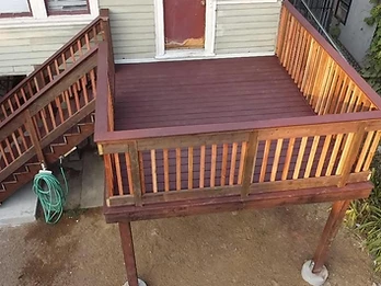 High-angle view of raised wooden deck with dark stain, alternating-tone balusters, and staircase descending to concrete patio on footings
