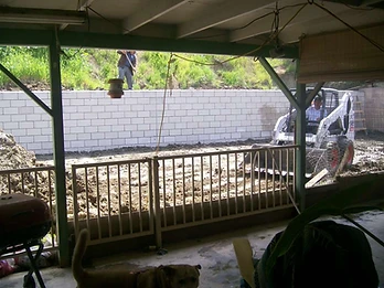 Construction site with retaining wall, skid-steer loader, and worker with shovel viewed from a covered patio
