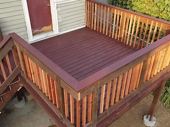 Elevated high-angle shot of a completed wooden deck with dark reddish-brown planks, railing, and staircase on concrete footings