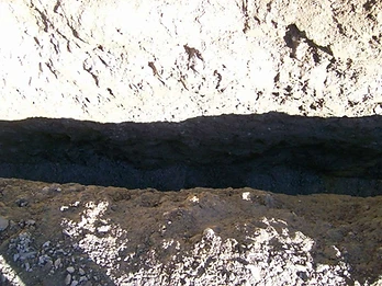Top-down view of a narrow excavated trench with layered earth banks and compacted soil base