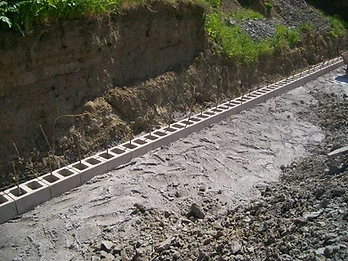 Concrete masonry blocks and vertical rebar prepared for a retaining wall foundation on a hillside site