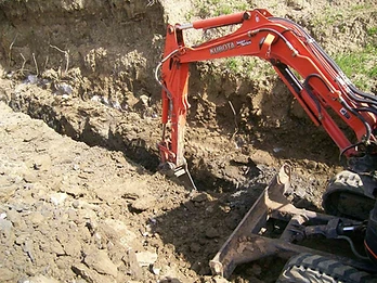 Orange Kubota Super Series excavator digging a narrow trench with vertical rebar rods visible in the excavation