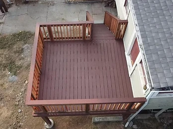 High-angle view of completed elevated wooden deck with dark reddish-brown stain and natural wood balusters against pale siding