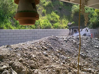 Concrete block retaining wall with skid-steer loader and excavated dirt pile on a hillside site