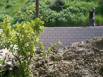 Concrete block retaining wall under construction with excavated soil and hillside behind