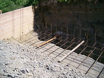 High-angle view of rebar grid in a foundation trench with vertical starter bars and wooden support beams for a retaining wall