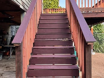Newly constructed wooden staircase with dark reddish-brown treads and natural cedar balusters leading up to an elevated deck