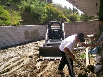 Worker leveling a concrete block retaining wall with a skid-steer loader nearby