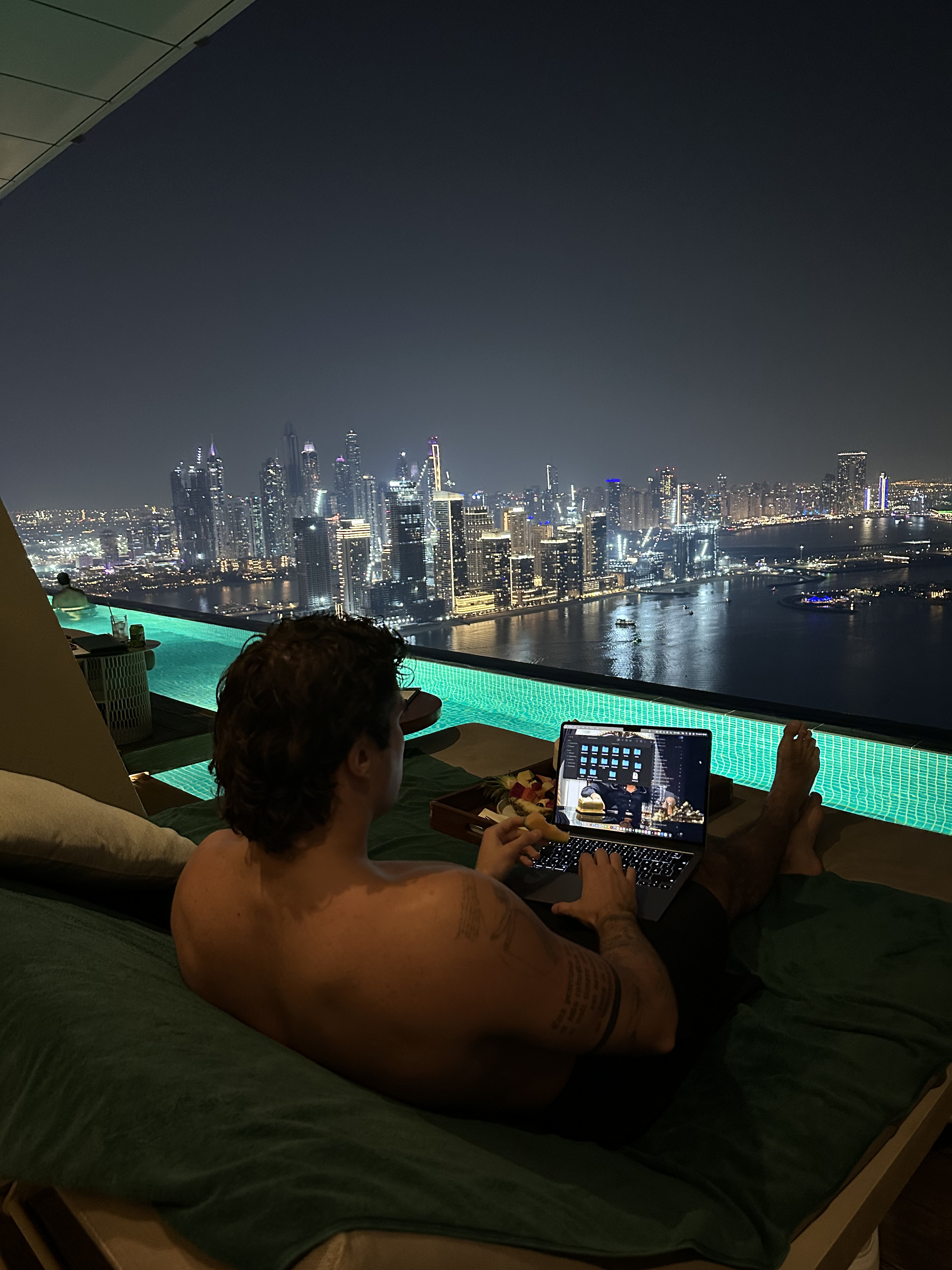 Working from a poolside lounge at night, city skyline in the background