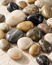 Objets & Fleurs — close-up of polished natural stones in cream, tan, grey, and black that anchor each permanent orchid composition in its vessel
