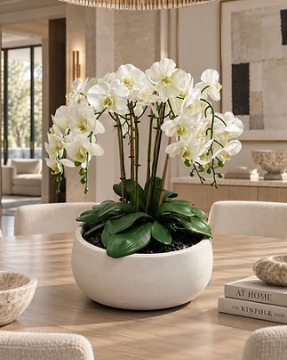 Objets & Fleurs — white permanent Phalaenopsis orchid composition in a cream vessel beside art books in a bright modern luxury living room