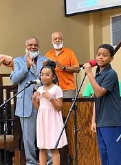 Children singing and speaking at microphones during a youth service