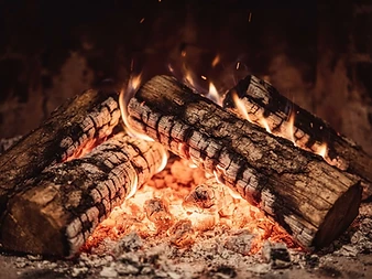Seasoned hardwood stacked beside a glowing coal bed