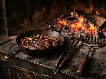 Cast-iron skillet, long tongs, and a grill rake laid out for live-fire cooking