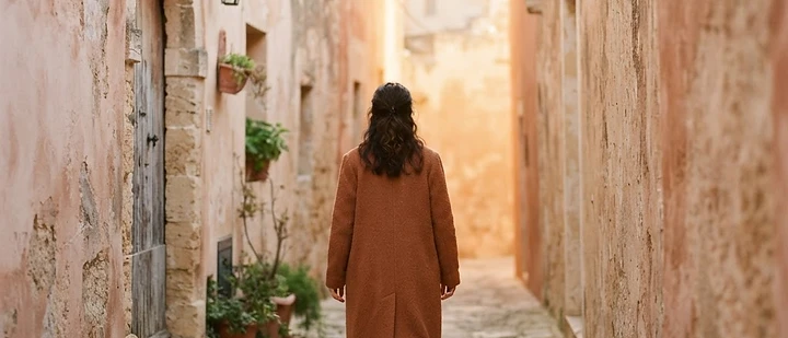 A woman walking down a quiet sunlit lane between warm walls