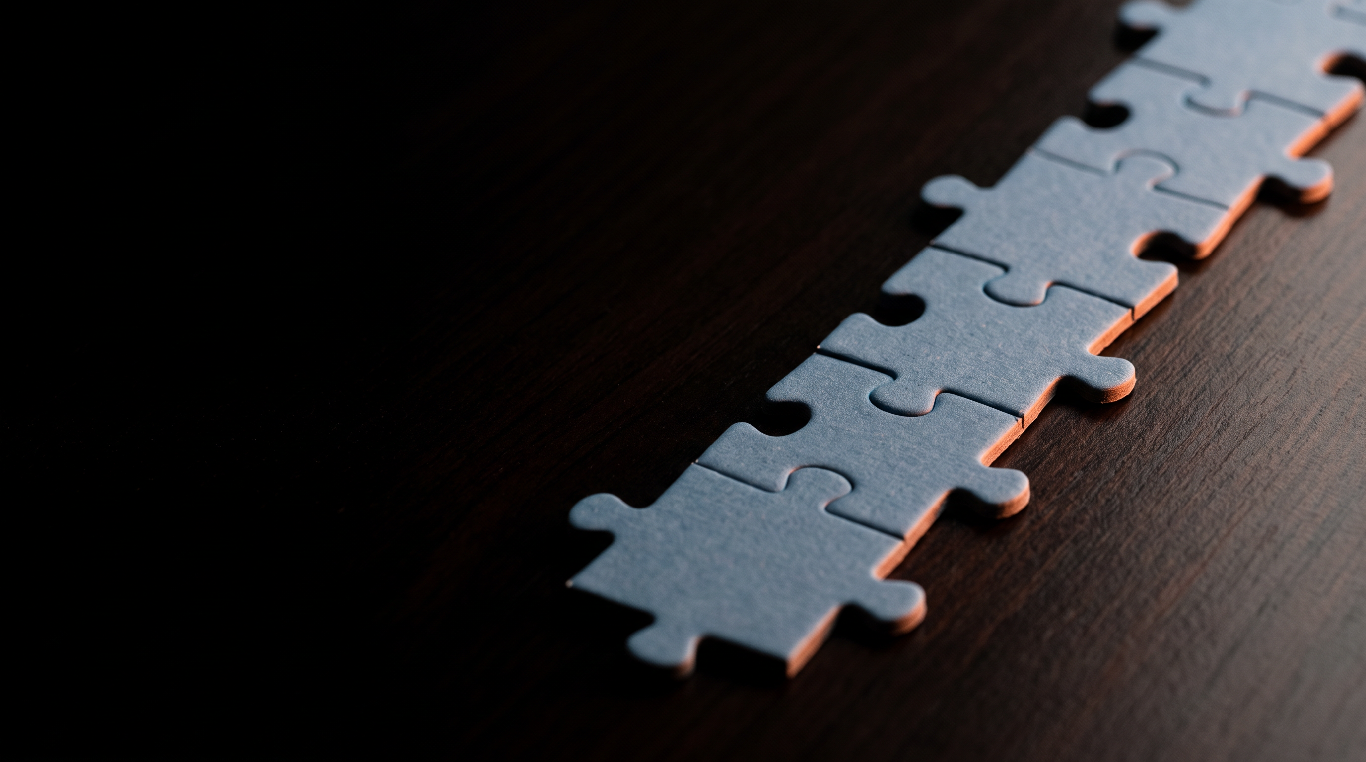 Jigsaw puzzle pieces laid in a precise straight row beside a blank brass straightedge under one raking light
