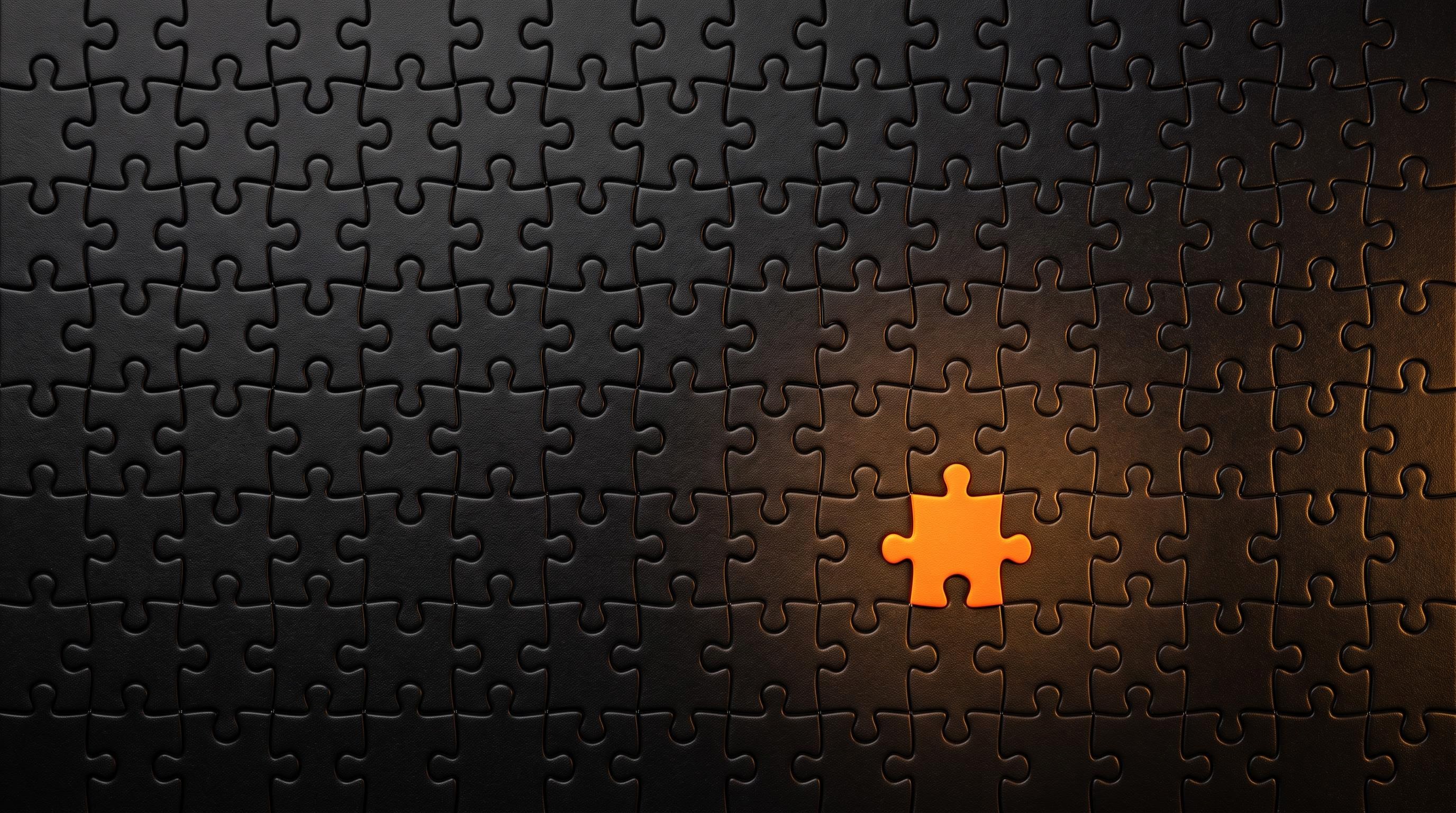 A close-up of matte-black interlocking jigsaw puzzle pieces filling the frame on a black table, with one orange piece catching warm light