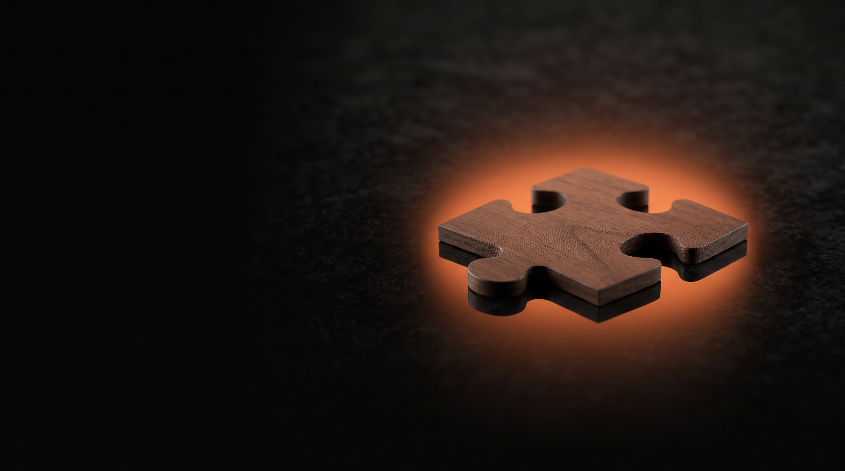 A jigsaw puzzle piece resting on polished black stone with a faint reflection beneath it and a warm orange glow behind