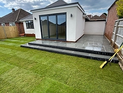 Grey stone patio with striped lawn and white-rendered extension