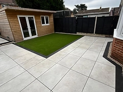 Large-format light-grey porcelain patio with artificial lawn and brick wall