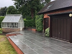 Dark slate-style paved patio with low brick edge and Victorian greenhouse