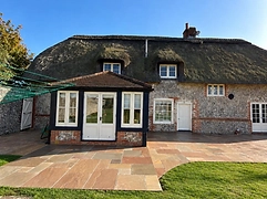 Mixed-stone patio in earthy tones beside a thatched cottage