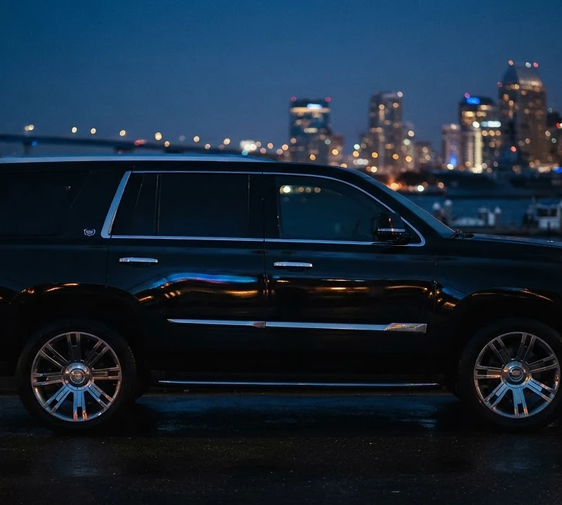 Black Cadillac Escalade at dusk with San Diego harbor lights