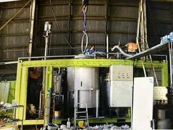 Workers assembling a lime-green frame around a stainless vessel with crane lifting gear