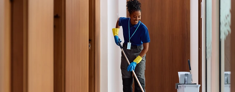 Cleaning supplies in the foreground while professional cleaners service a modern office.