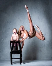 Young dancer leaping beside a toddler in a pink tutu