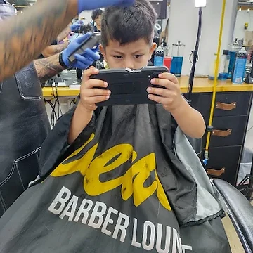 Young boy getting a haircut in a Seven18 branded cape