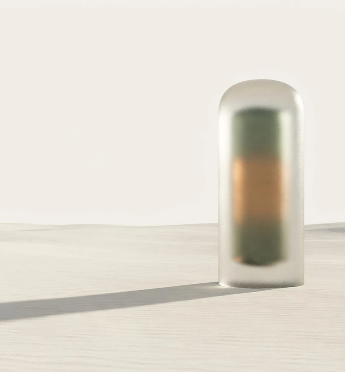 Un pilier de verre givré dressé dans un désert de sable crème, baigné d’une lumière bronze et vert sauge