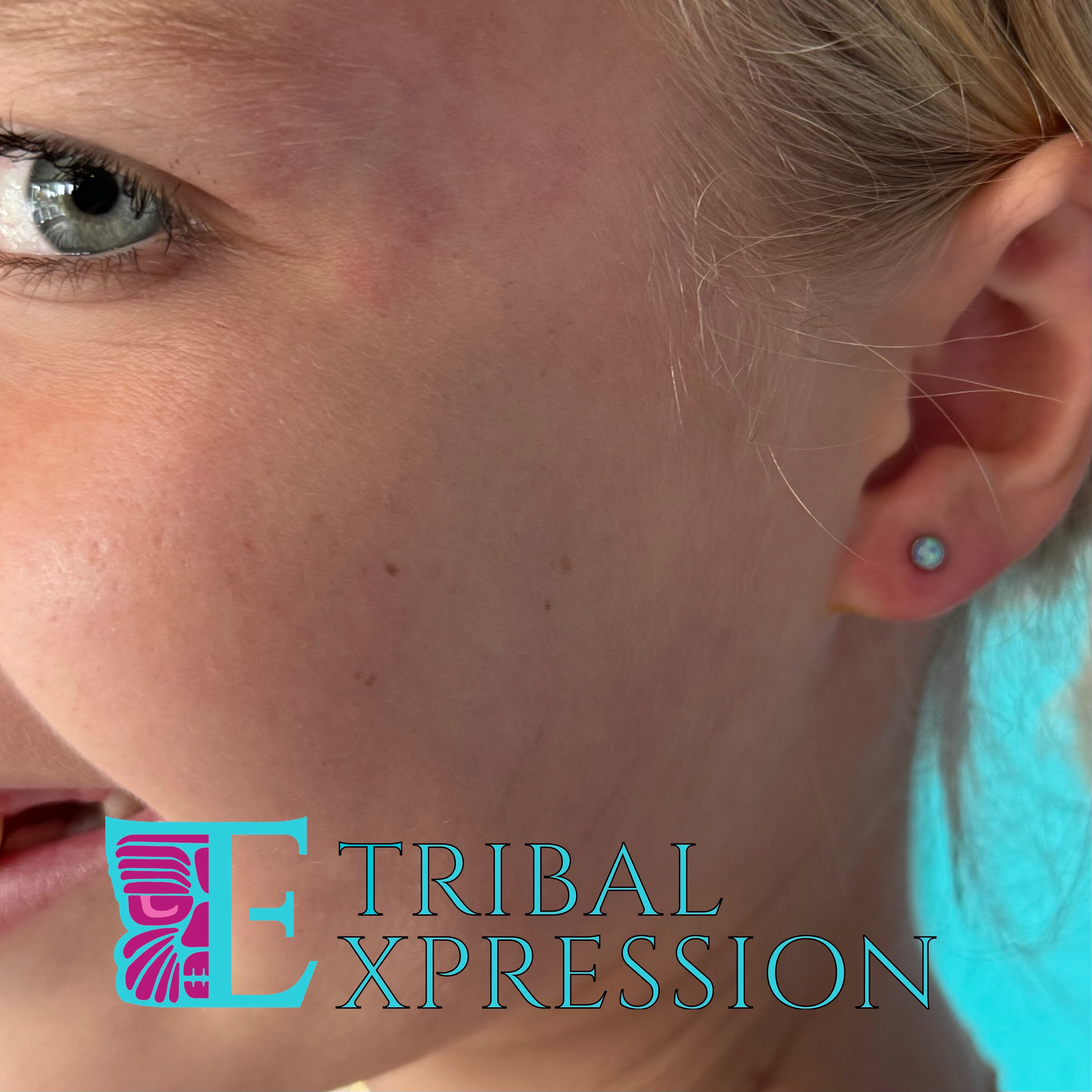 A child's ear with a light-blue gemstone stud earring in the earlobe.