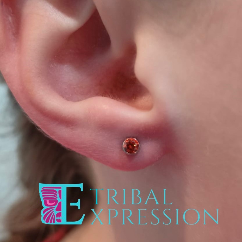 A child's ear with a bright orange gemstone stud earring in the earlobe.
