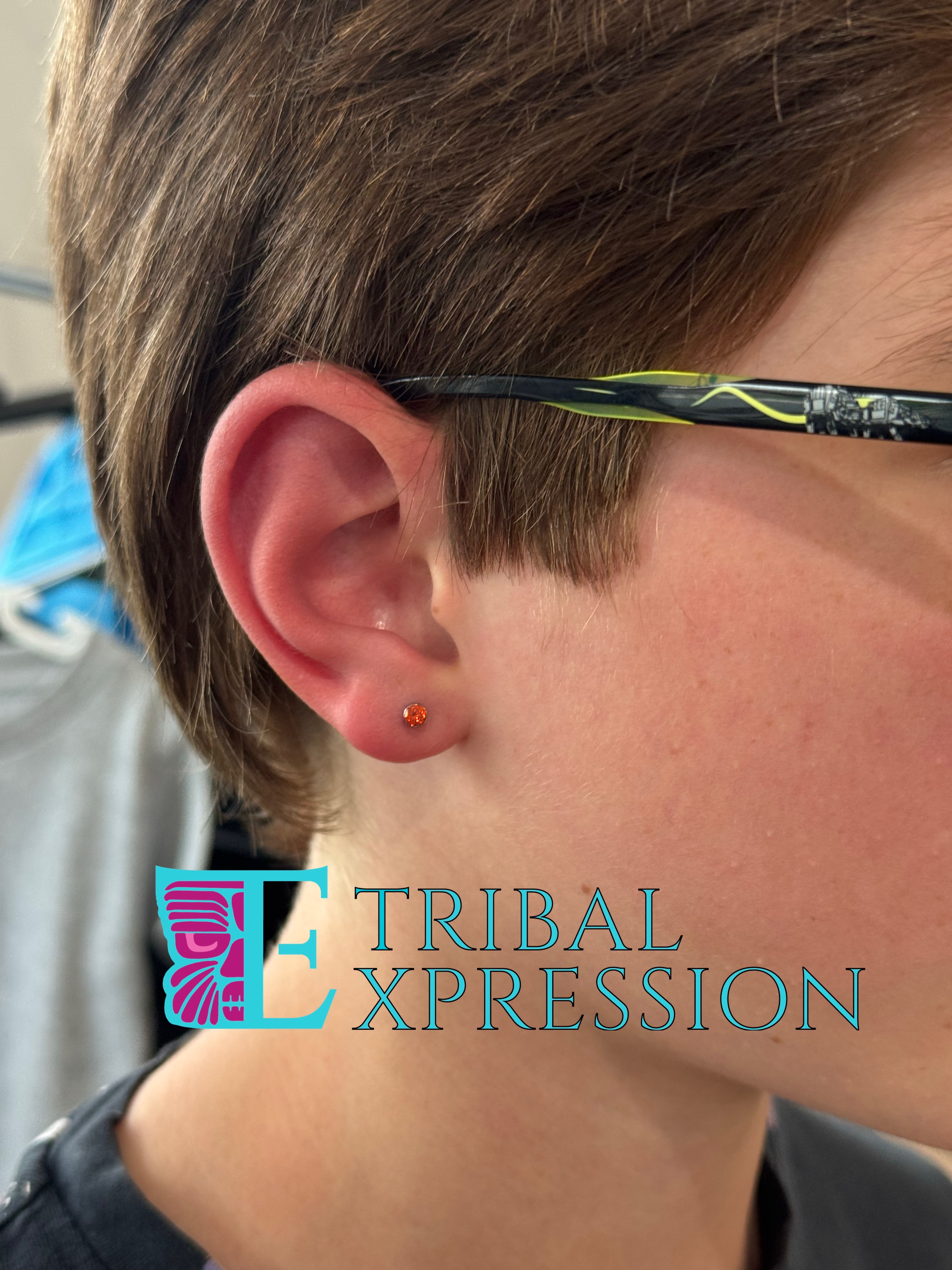 A person's ear with a small amber-orange spherical stud earring in the earlobe.